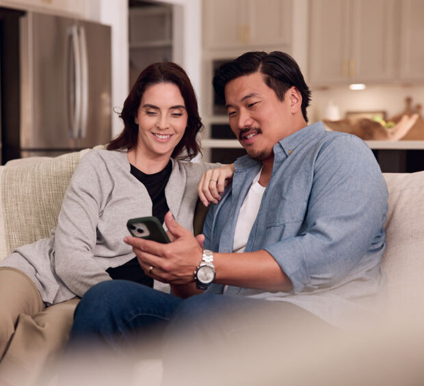Two people looking at a phone together on a couch at home