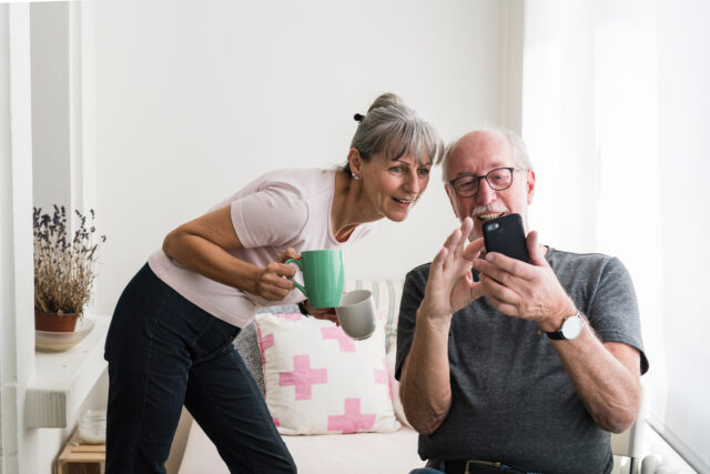 Older couple looking at a phone together, one holding a mug